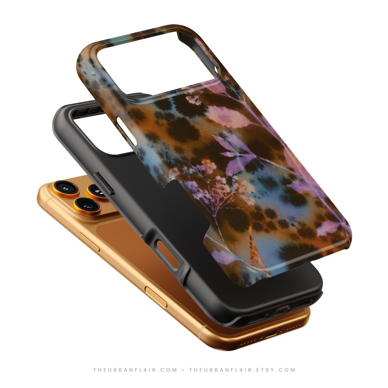Puede incluir: Un tel&eacute;fono inteligente dorado colocado bajo una funda protectora negra con un dise&ntilde;o floral decorativo en tonos marr&oacute;n, azul y morado. La funda tiene recortes para la c&aacute;mara y los botones laterales, mostrando un dise&ntilde;o en capas.