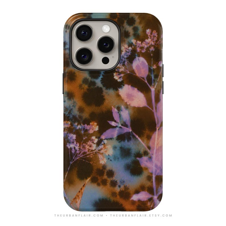 Puede incluir: Una funda para smartphone con fondo tie-dye en azul y marr&oacute;n oscuro, con un estampado bot&aacute;nico de flores silvestres y hojas en color violeta claro. La funda tiene un recorte para una c&aacute;mara de triple lente e incluye el texto THEURBANFLAIR.COM.