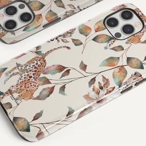 Pu&ograve; includere: Una custodia per telefono beige con un design a stampa leopardata e foglie ad acquerello. La custodia presenta un effetto glitter dorato e il testo "URBANRAIA" in basso.