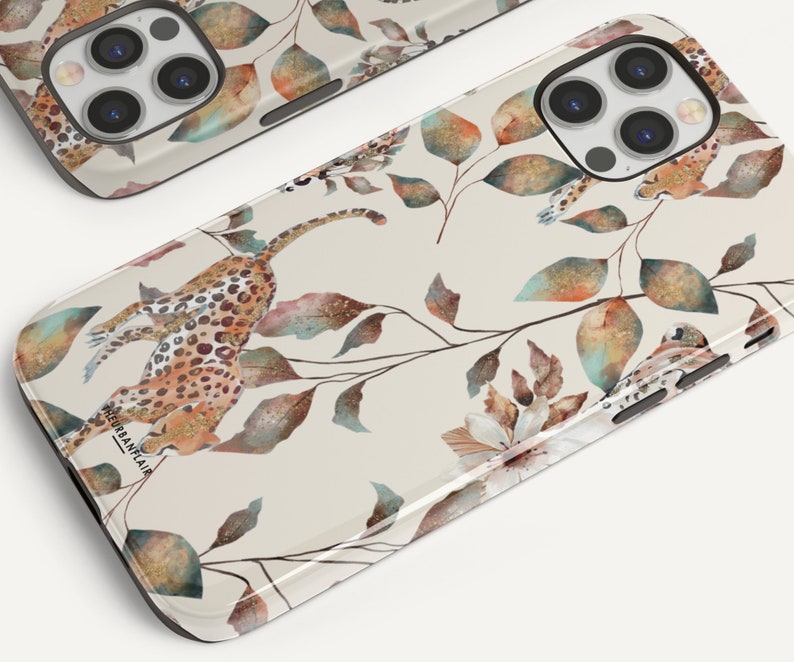 Pu&ograve; includere: Una custodia per telefono beige con un design a stampa leopardata e foglie ad acquerello. La custodia presenta un effetto glitter dorato e il testo "URBANRAIA" in basso.