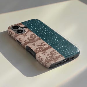 May include: A rectangular smartphone case featuring a dual-pattern design. One section displays a beige lace-like floral pattern, while the other is a dark teal surface covered in small white dots. The case includes cutouts for the camera and ports.