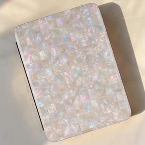 Op de afbeelding: Een rechthoekig etui met een mozaïek van iriserende witte parelmoertegels. Het oppervlak toont een rasterpatroon met glinsterende roze, blauwe en gouden accenten. De tekst THEURBANFLAIR.COM staat gedrukt langs de linkerzijkant van het etui.