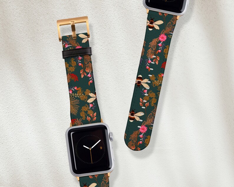 May include: Two Apple Watch bands with a green background and a floral pattern featuring bees and flowers. The bands are made of leather and have a gold buckle.