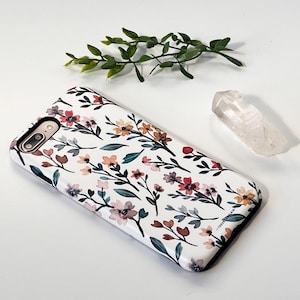 May include: A white phone case with a floral pattern featuring watercolor-style flowers in shades of pink, red, orange, and yellow. The flowers are arranged on a white background with dark gray stems and leaves.