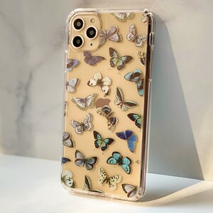 Op de afbeelding: Een transparante telefoonhoes met een gouden rand en een patroon van blauwe en witte vlinders op een cr&egrave;mekleurige achtergrond.