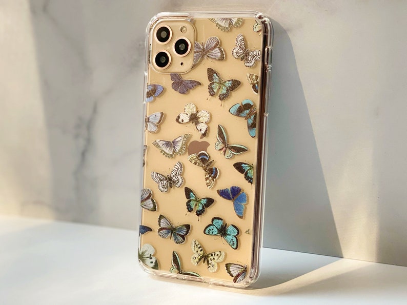 Op de afbeelding: Een transparante telefoonhoes met een gouden rand en een patroon van blauwe en witte vlinders op een cr&egrave;mekleurige achtergrond.