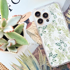 May include: Clear phone case with a botanical design featuring green leaves and stems. The case is on a white background and has a clear border. The phone case is next to a succulent plant in a white pot.