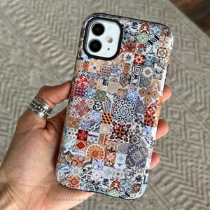 Könnte beinhalten: Eine Smartphone-Hülle mit einem lebendigen, mehrfarbigen Mosaikmuster aus verschiedenen geometrischen und floralen Fliesendesigns in Blau-, Rot-, Orange- und Weißtönen. Die Hülle hat einen schwarzen Kameraausschnitt und den Text THEURBANFLAIR.COM unten.