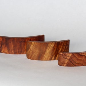 May include: Three wooden curved display stands made of reddish-brown wood with a natural wood grain pattern.