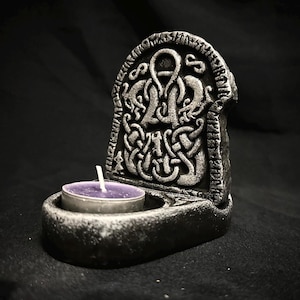 May include: A black candle holder with a Celtic knot design and a small purple candle inside.