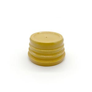 May include: A mustard yellow ceramic plant pot saucer with a circular shape and three distinct horizontal ridges along the side. The saucer features a smooth, glossy finish and a small drainage hole centered on the flat base of the interior surface.