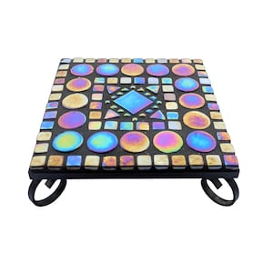 May include: Square mosaic tile tabletop with iridescent glass tiles in a variety of colours, including blue, yellow, and purple. The mosaic is set on a black metal base with curved legs. The tabletop measures approximately 25 cm square.