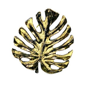 Puede incluir: Anillo de servilleta de metal de color dorado en forma de hoja de monstera tropical.