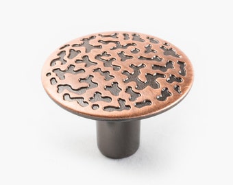 May include: A round, copper-colored cabinet knob with a black, intricate, patterned design. The knob has a short, black stem.