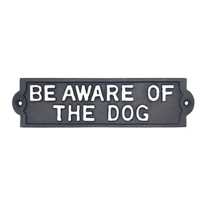 May include: Black metal sign with white lettering that reads "BE AWARE OF THE DOG".