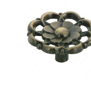 Puede incluir: Un pomo de armario decorativo de latón antiguo con un diseño floral. El pomo es redondo con un centro elevado y un patrón floral detallado.