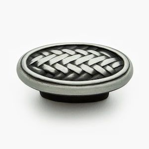 May include: An oval-shaped cabinet knob with a woven design in a silver finish. The knob has a raised edge and a black center.
