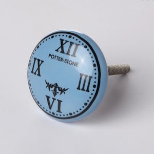 May include: A light blue ceramic knob with a black clock face design. The clock face features Roman numerals and the text "POTTER-STONE".
