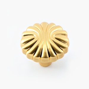 May include: A gold-toned cabinet knob with a scalloped design. The knob has a smooth, shiny finish.