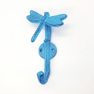 May include: A light blue cast iron dragonfly hook. The hook is shaped like a dragonfly with a curved hook at the bottom.