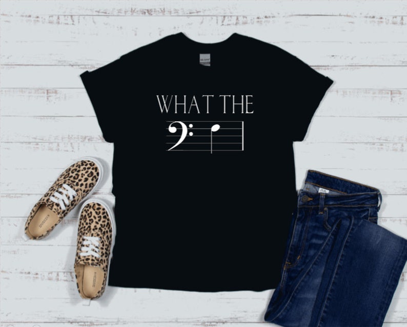 以下が含まれることがあります： 「WHAT THE」というテキストと五線譜に書かれた音符がプリントされた黒いTシャツ