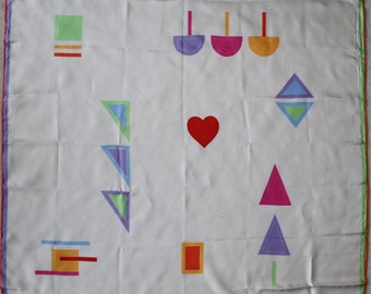 May include: White silk scarf with a colorful geometric design. The design includes a heart, triangles, squares, and rectangles in shades of red, pink, orange, yellow, green, blue, and purple.