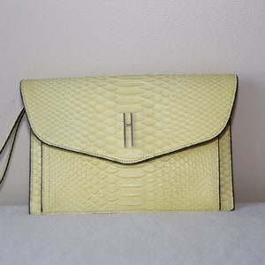 May include: A pale yellow snakeskin clutch with a silver H clasp.