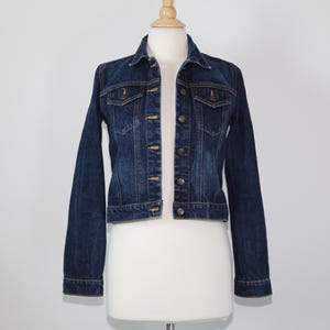 May include: A dark blue denim jacket with a classic design. The jacket features a button-up front, two chest pockets, and long sleeves. The jacket is displayed on a mannequin against a plain white background.