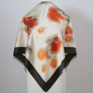May include: Square silk scarf with a cream background and a floral pattern in shades of red, orange, and gray. The scarf has a dark green border.
