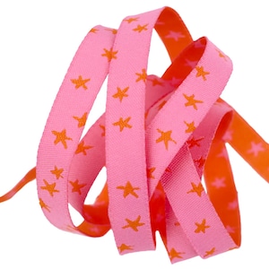 May include: Pink ribbon with orange star print. The ribbon is folded and twisted, showing the pattern on both sides.
