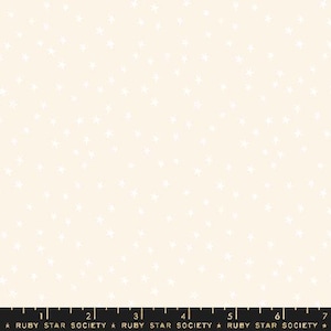 May include: A white fabric with a repeating pattern of small white stars on a cream background. The fabric has a ruler at the bottom with the text "Ruby Star Society" printed on it.