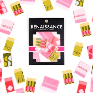 May include: A collection of decorative ribbons and trims with the "Renaissance Ribbons & Trims" logo. The ribbons are in various colors, including pink, green, and yellow, with text such as "hi", "hey", and "handmade".