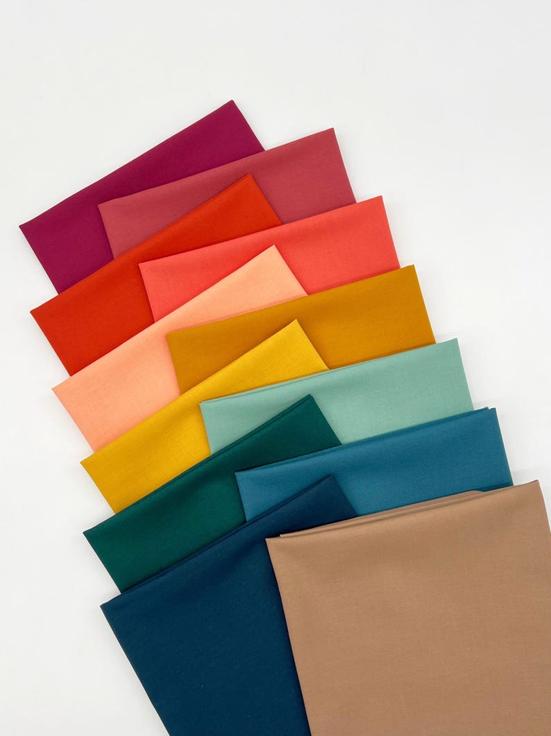 May include: A collection of rectangular fabric swatches arranged in a fan-like pattern. The colors include shades of magenta, red, orange, peach, yellow, mustard, mint green, teal, dark blue, and a solid tan square at the bottom right.