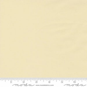May include: A solid cream colored fabric swatch with a ruler showing 6 inches. The ruler has the word "moda" printed on it.