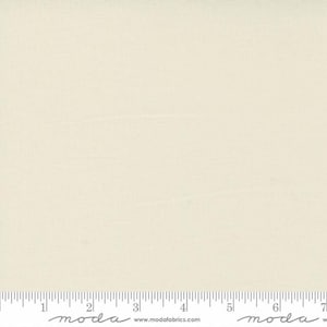 May include: A solid off-white fabric swatch with a subtle texture. The fabric is measured in inches with a ruler that reads "moda" at the 2-inch and 6-inch marks.