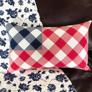 May include: A rectangular throw pillow featuring a diagonal gingham check pattern in red, white, and navy blue. The design mimics a flag layout with a navy blue and white checkered canton section on the left and red and white checks throughout.