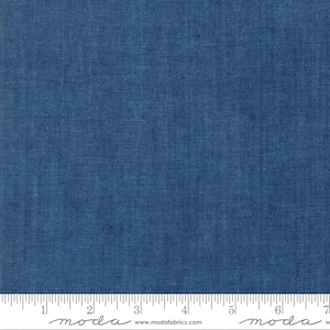 May include: A close-up of a solid blue fabric with a textured woven pattern. The fabric is measured with a ruler in inches. The ruler has the word "moda" printed on it.