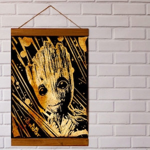 May include: A framed print of a golden Groot character from the Guardians of the Galaxy movie series. The background is black with gold streaks and dots. The print has the text "I am Groot" in gold lettering.