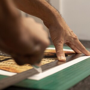Puede incluir: Una mano utiliza una regla y un c&uacute;ter para cortar un trozo de papel con un dise&ntilde;o impreso en una estera de corte verde.