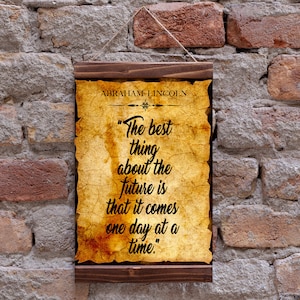 May include: A wooden framed print with a vintage parchment background featuring a quote by Abraham Lincoln: "The best thing about the future is that it comes one day at a time."