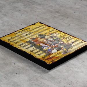 May include: A framed print with sheet music and the text "Dearly Beloved", alongside a colourful illustration of characters. The print has a distressed, aged look and is set in a black frame.
