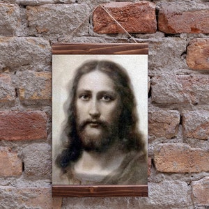 May include: A framed print of a black and white image of Jesus Christ. The image is a close-up of his face and shoulders. The frame is made of dark wood.