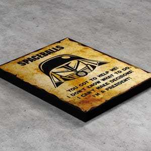 Könnte beinhalten: Ein rechteckiges Holzschild mit schwarzem Rand und einem Hintergrund in Papieroptik. Das Schild zeigt eine schwarze Grafik eines Helms und den Text "SPACEBALLS" und ein Zitat. Das Schild ist eine Parodie eines berühmten Films.