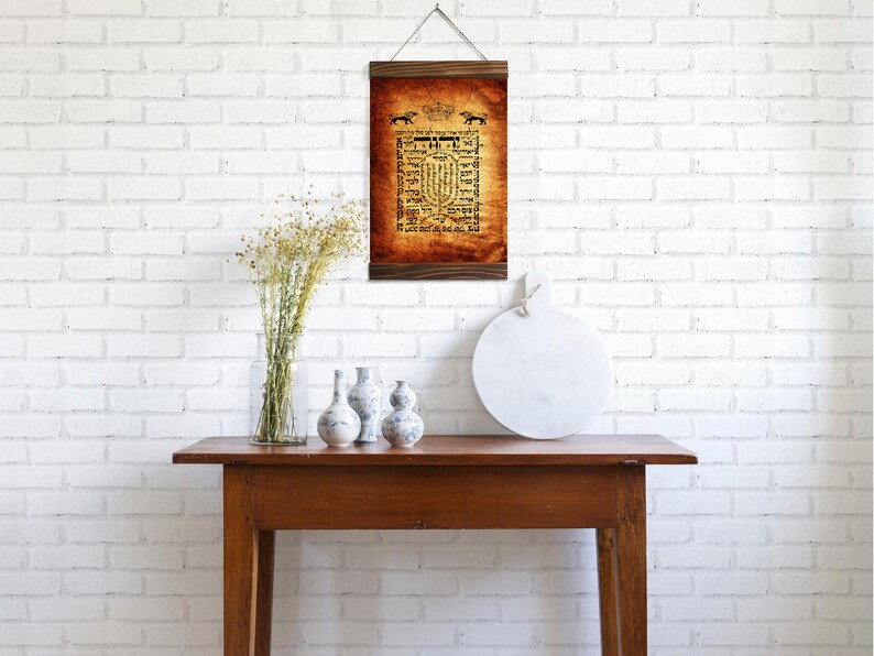 Puede incluir: Una impresi&oacute;n enmarcada con una est&eacute;tica vintage que presenta texto en hebreo y un borde decorativo. La impresi&oacute;n est&aacute; colgada en una pared de ladrillo blanco sobre una mesa de madera con una bandeja redonda de m&aacute;rmol blanco y tres jarrones decorativos.