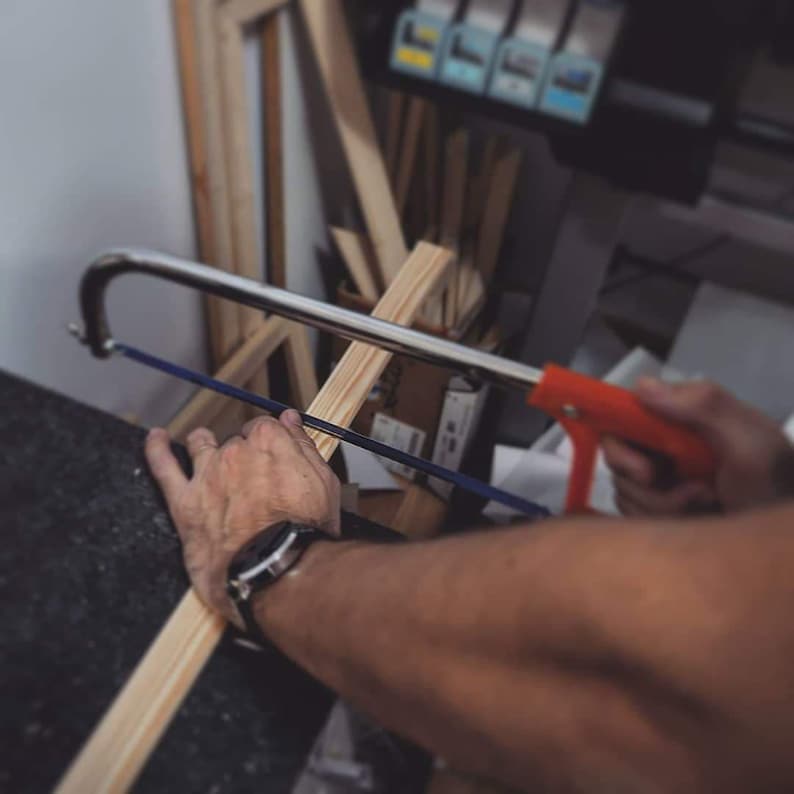 Puede incluir: Una persona utiliza una sierra de mano para cortar un trozo de madera. La sierra tiene un mango rojo y una hoja azul. La madera es de color marr&oacute;n claro y tiene una textura rugosa.