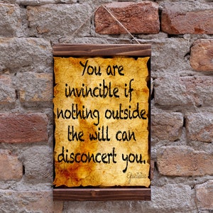 Op de afbeelding: Een houten ingelijst bord met een vergeelde perkament achtergrond. Het bord toont de tekst "You are invincible if nothing outside the will can disconcert you." De quote wordt toegeschreven aan Epictetus.