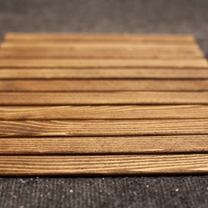 Puede incluir: Un posavasos de madera con un acabado marr&oacute;n natural. El posavasos est&aacute; hecho de finas piezas rectangulares de madera que est&aacute;n dispuestas en un patr&oacute;n de cuadr&iacute;cula.