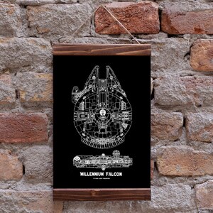 Op de afbeelding: Een zwart-witte blauwdruk-stijl illustratie van het ruimteschip Millennium Falcon op een zwarte achtergrond. De afbeelding is ingelijst in een donkerhouten lijst.
