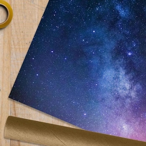 May include: A close-up of a blue and purple starry night sky wrapping paper. The paper is rolled up and ready to be used.