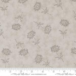 May include: A light beige fabric with a subtle mottled texture. The fabric features a repeating pattern of delicate, stylized dandelion seed heads in a muted gray-brown color. A ruler with inch measurements is visible along the bottom edge.